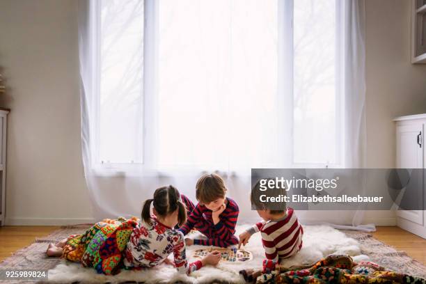 three children lying on the floor playing a board game - game board stock pictures, royalty-free photos & images