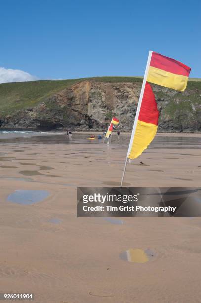 red and yellow lifeguard on patrol flag on an empty beach - mawgan porth stock pictures, royalty-free photos & images
