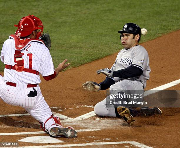 Johnny Damon of the New York Yankees gets hit by the ball as he slides safely into home on a sacrifice fly by Jorge Posada ahead of the throw to...
