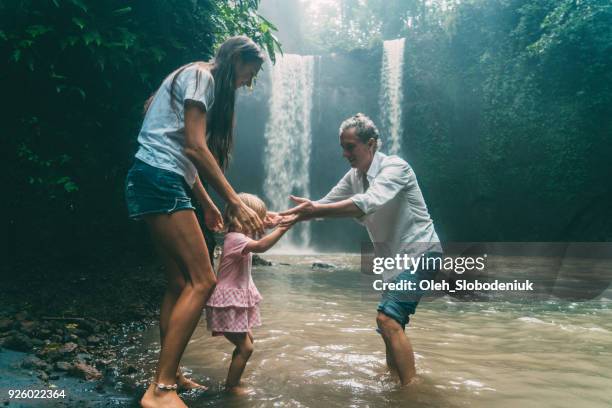 mother and father playing with daughter near waterfall - bali waterfall stock pictures, royalty-free photos & images