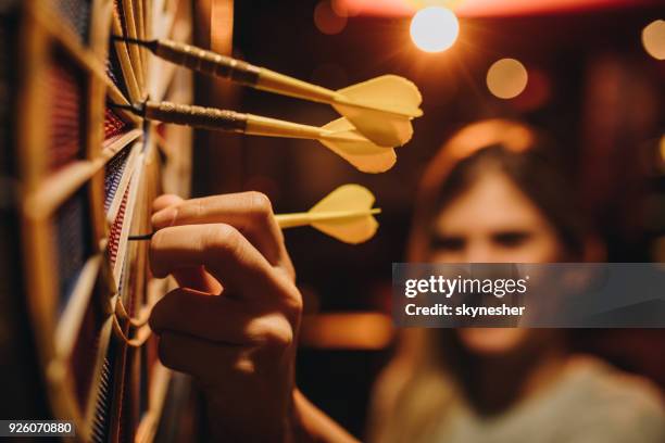 nahaufnahme einer frau die darts aus dartscheibe. - dart board stock-fotos und bilder