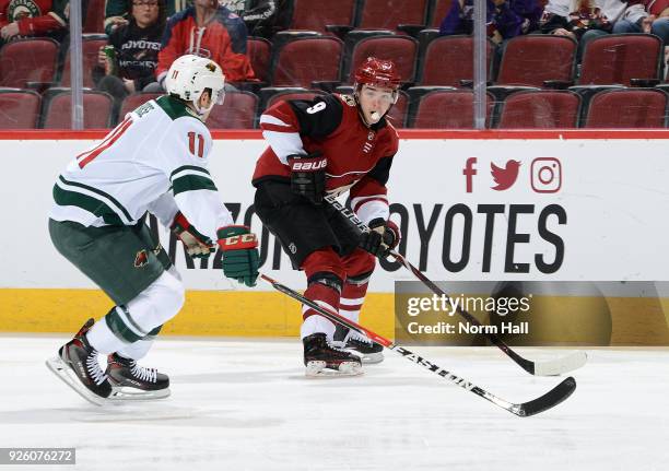 Clayton Keller of the Arizona Coyotes skates with the puck ahead of Zach Parise of the Minnesota Wild during the first period at Gila River Arena on...