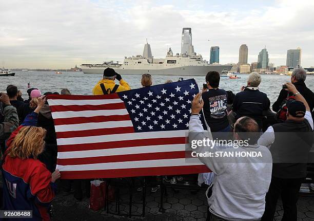 People wave an American flag as the USS New York enters New York harbor Novermber 2, 2009 on its way past the former World Trade Center site. The US...