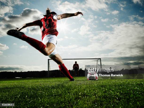 female soccer player kicking ball toward goal - girls football stockfoto's en -beelden