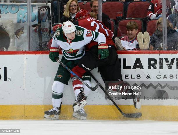 Derek Stepan of the Arizona Coyotes is checked into the boards by Tyler Ennis of the Minnesota Wild during the third period at Gila River Arena on...