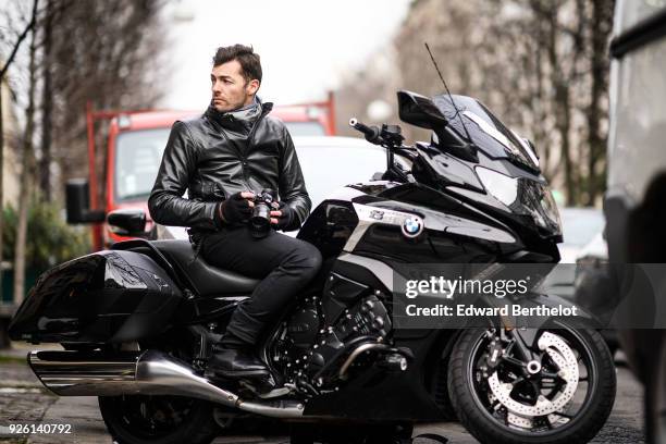 Photographer Francois Xavier Watine wears a black leather jacket and is using a Sony Alpha 7r iii mirrorless camera, on a BMW black motorbike, during...