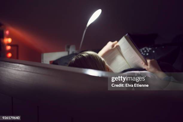 child reading bedtime book lit by night light - bedtime story book stock pictures, royalty-free photos & images