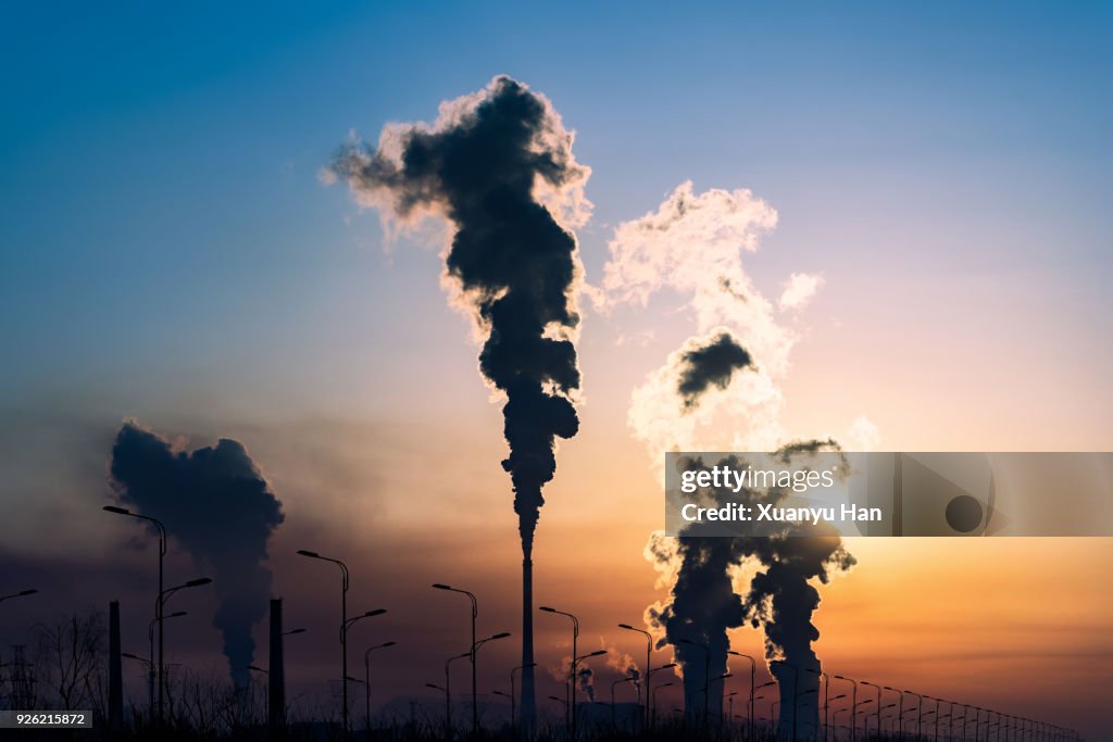 Silhouette of a high industrial pipe with the sun behind it