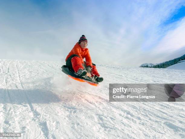 young boy going down a hill with a toboggan and getting airborne after jumping on a bump - sledge fotografías e imágenes de stock