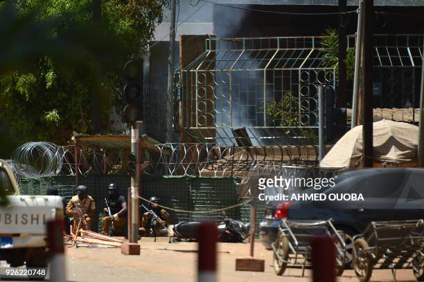 Security personnel take cover as smoke billows from The Institute Francais in Ouagadougou on March 2 as the capital of Burkina Faso came under...