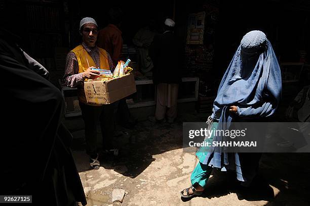 An Afghan caries his wares as a burqa-clad woman walks in the old city of Kabul on July 6, 2009. Afghans go to the polls on August 20 to elect a...