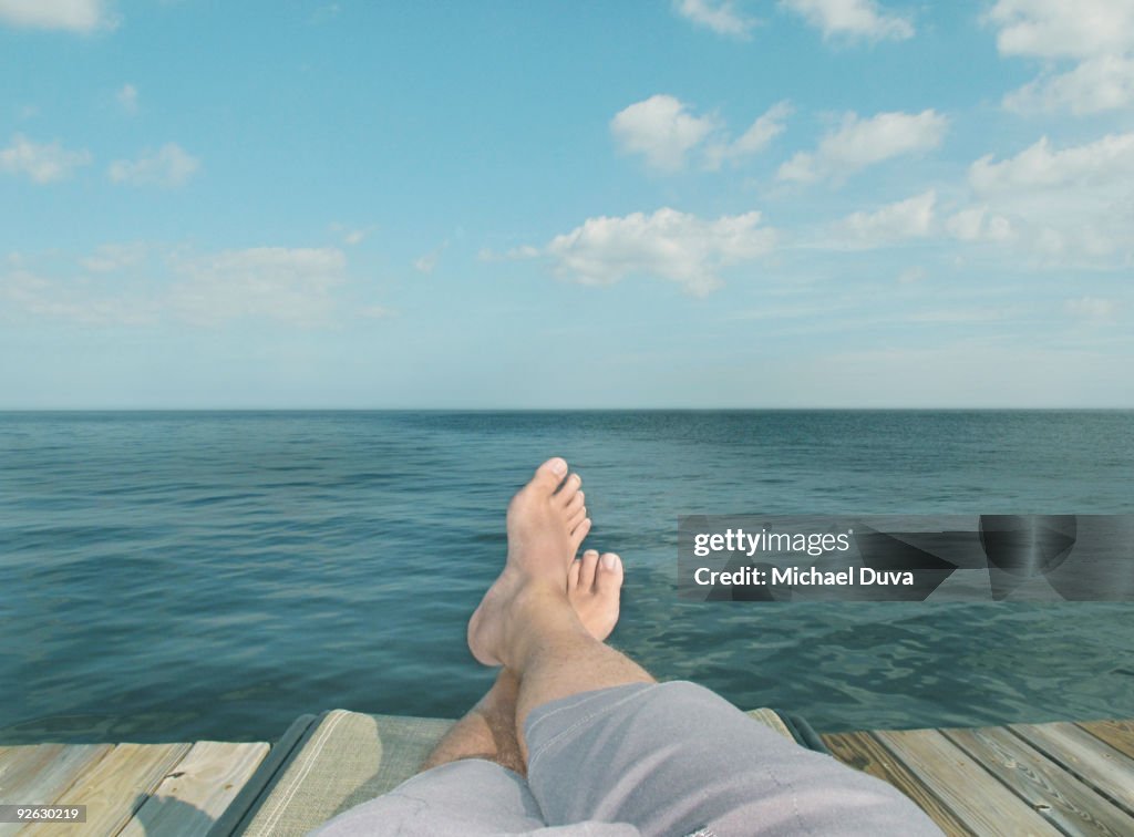 Detail of feet relaxing on chair in front of water