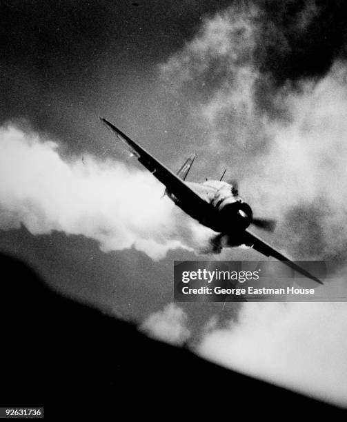 View of an American fighter plane, with smoke billowing out from under its left wing, during fighting over the Pacific in World War II, ca.1944.