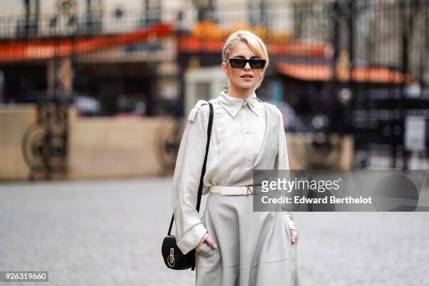 Caroline Daur wears a gray dress, a belt, a black bag, sunglasses, black shoes, and attends the Nina Ricci show as part of the Paris Fashion Week...