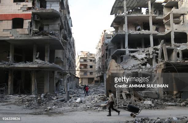 Syrian youth pulls a cart as he walks down a street past destroyed buildings in the rebel-held besieged town of Ayn Tarma in the eastern Ghouta...