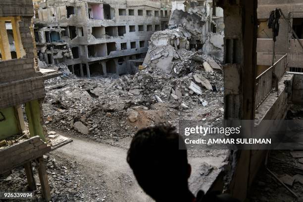 Picture taken on March 2, 2018 shows a Syrian youth looking through a balcony from a severely damaged building at the exposed painted walls of rooms...