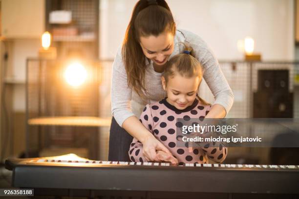 joven madre enseñando a su hija a tocar piano eléctrico - electric piano fotografías e imágenes de stock