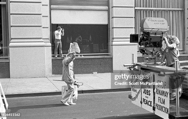 New York - An elderly man dressed as Uncle Sam waves American Flags, as a laborer stands with a mock movie camera in downtown Manhattan. They are...