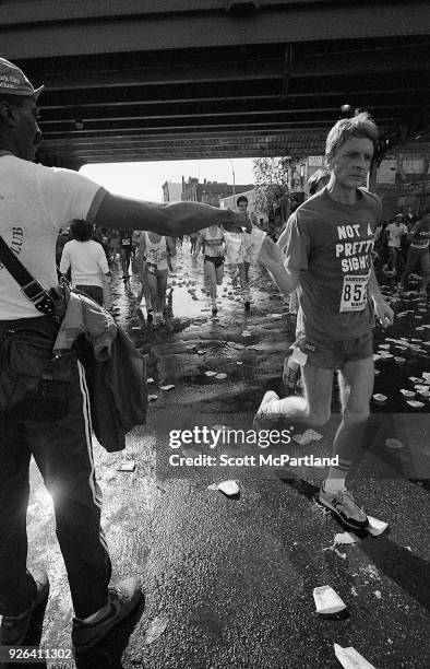 New York - A volunteer with the New York Road Runners Club hands a cup of water to a runner at the 10 mile mark on Bedford Avenue in Brooklyn during...