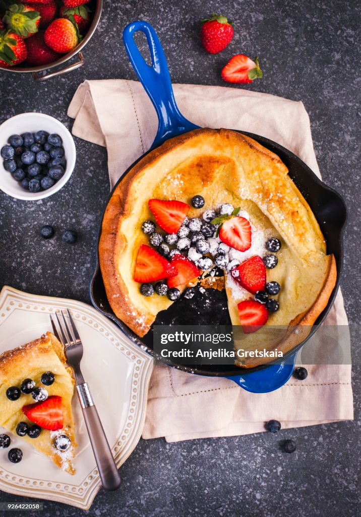Dutch Baby Pancakes with berries and powdered sugar baked in oven on iron pan