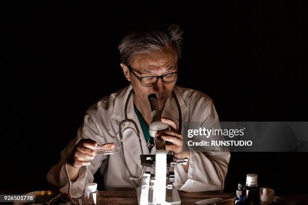 middle-aged doctor examining something through microscope - laboratory microscope stock pictures, royalty-free photos & images