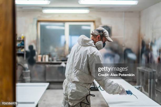 de volwassen man, arbeider, draagt de beschermend masker en overall, reinigen van oppervlakken voor schilderen met de samengeperste luchtpistool - air pollution mask stockfoto's en -beelden