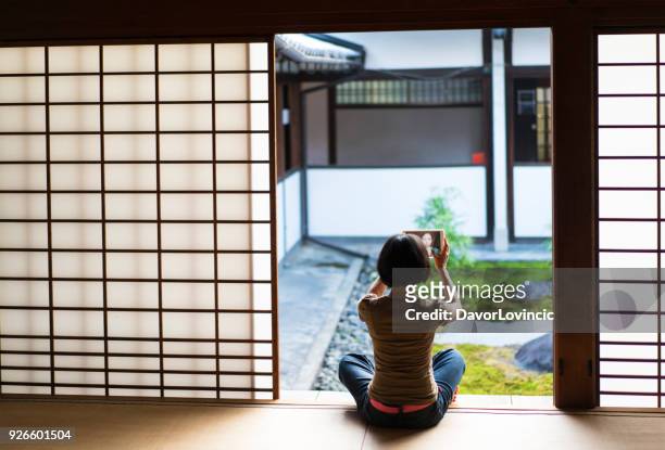 achteraanzicht van de vrouw zit op het podium van de tempel en het nemen van selfie met mobiele tablet terwijl u geniet van de chion.ji tempel zen tuin in kyoto, japan - chion in stockfoto's en -beelden