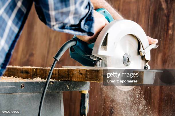 hombre carpintero con sierra circular eléctrica en taller casero astillas volando - herramienta eléctrica fotografías e imágenes de stock