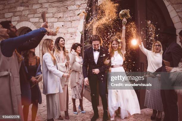 jonggehuwde paar lopen uit kerk en vieren de bruiloft met confetti - trouwerij stockfoto's en -beelden