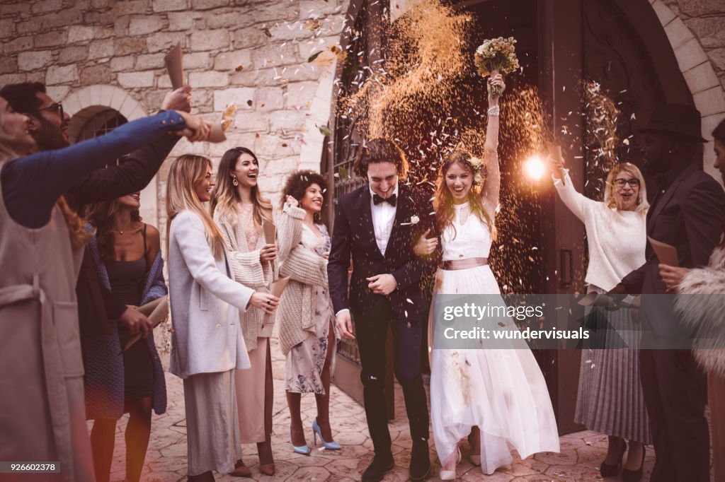 Newlywed couple walking out church and celebrating wedding with confetti