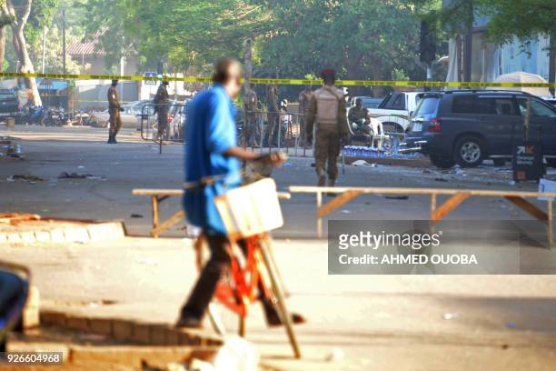 Cyclist watches military personnel outside the headquarters of the country's defence forces in Ouagadougou on March 3, 2018 a day after dozen of...