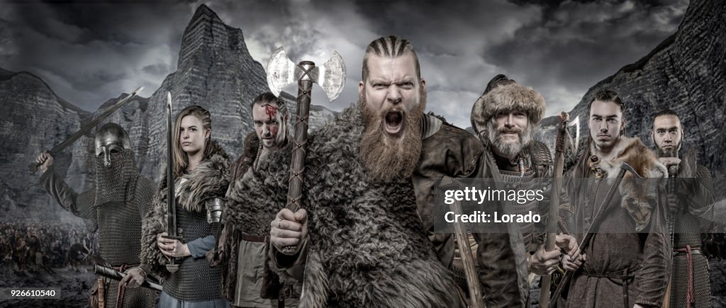 Weapon wielding viking warriors in formation in front of viking hoard and mountain range