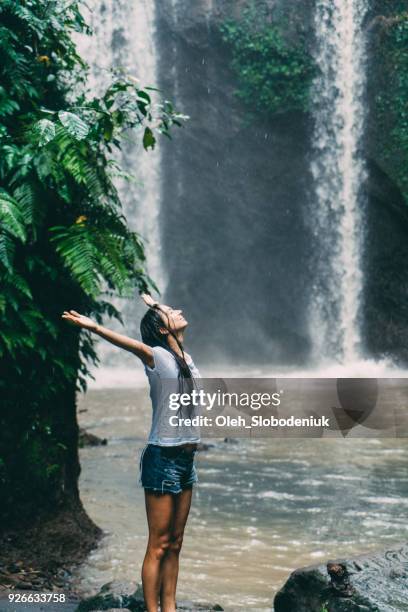 woman  in white shirt standing near  tibumana   waterfall under the rain  in bali, indonesia - rainy season stock pictures, royalty-free photos & images