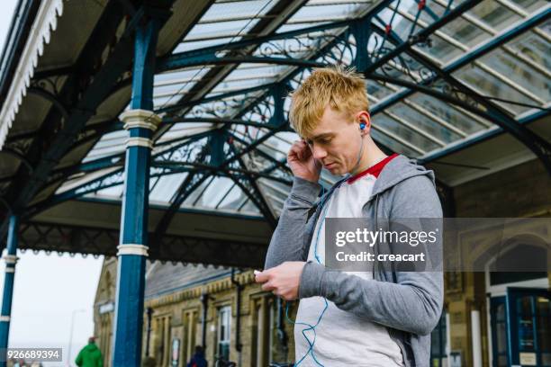 young man listening music outside a uk train station. - aparelho eletrónico de escuta imagens e fotografias de stock