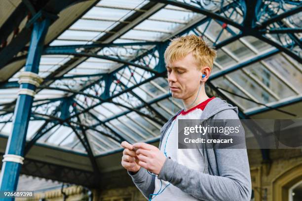 young man listening music outside a uk train station. - aparelho eletrónico de escuta imagens e fotografias de stock