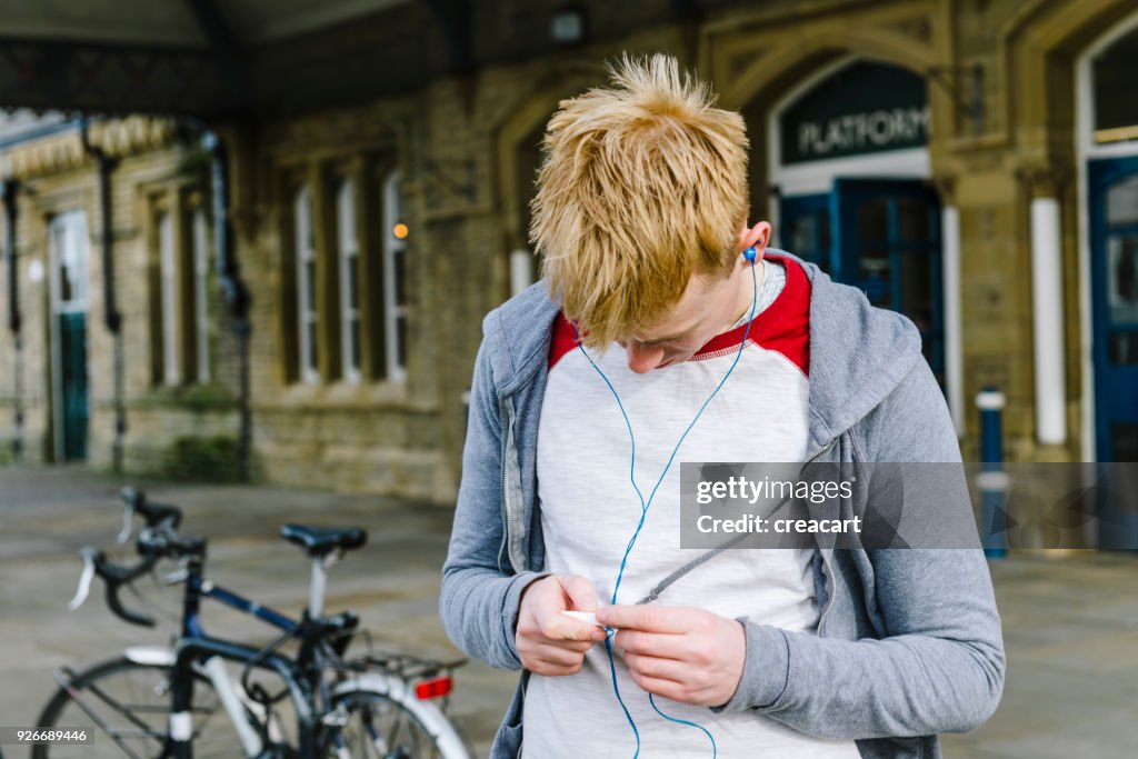 Young man listening music outside a UK Train Station.