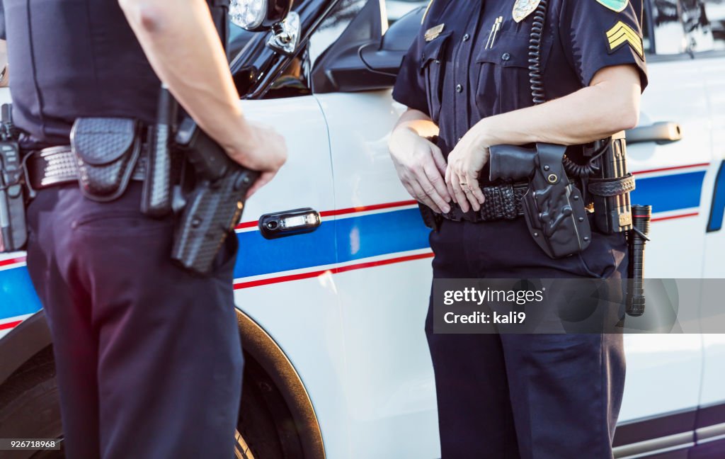 Policial e parceiro ao lado da viatura