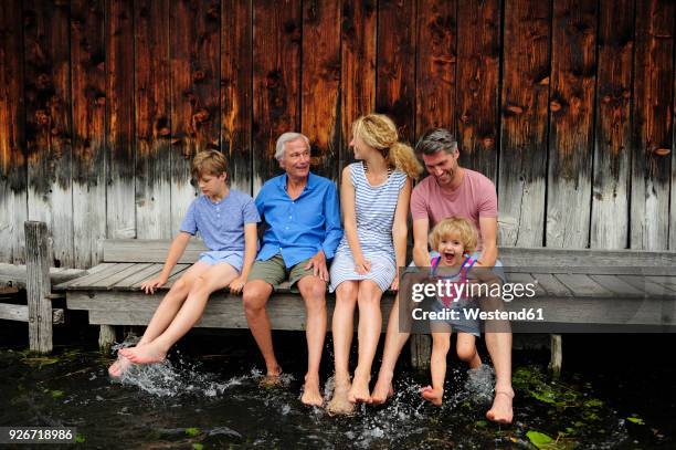 family sitting together on jetty splashing with water - boathouse stock pictures, royalty-free photos & images