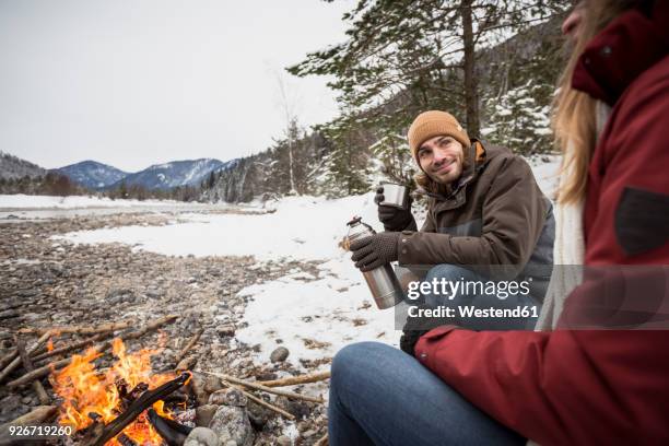 couple on a trip in winter having a hot drink at camp fire - tea hot drink - fotografias e filmes do acervo