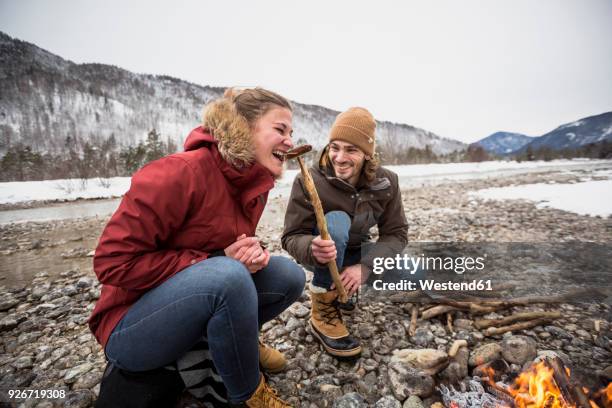 happy couple on a trip in winter eating a sausage at camp fire - food ready to eat stock pictures, royalty-free photos & images