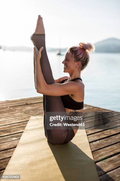 smiling woman practicing yoga on jetty at a lake - beugen oder biegen stock-fotos und bilder