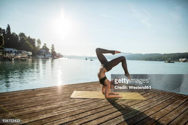 woman practicing yoga on jetty at a lake - yoga stock-fotos und bilder