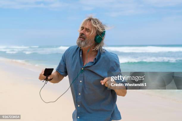 handsome senior man with headphones dancing on the beach - bali dancing stock pictures, royalty-free photos & images