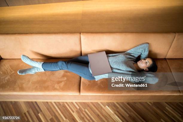 woman with laptop relaxing on couch - ambient light stock pictures, royalty-free photos & images