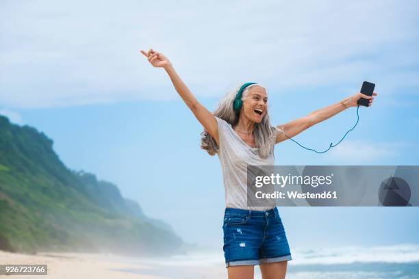 senior woman with headphones dancing on the beach - beautiful woman gray hair stock pictures, royalty-free photos & images