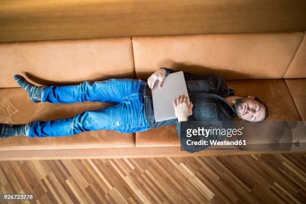 man with laptop relaxing on couch - ambient light stock pictures, royalty-free photos & images