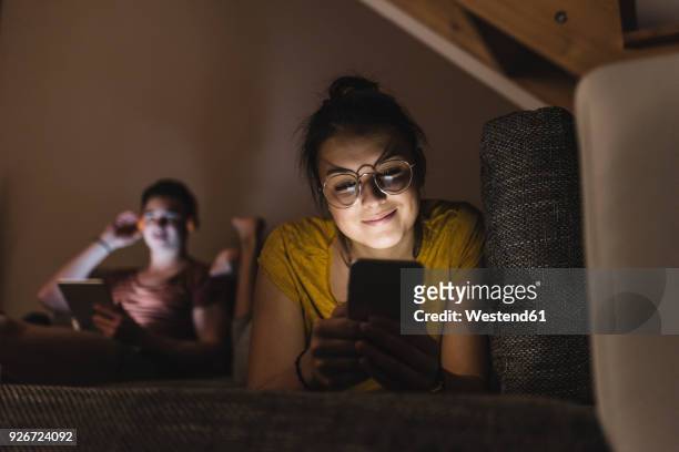 couple with cell phone and tablet relaxing on couch at home - woman enjoying night stock-fotos und bilder