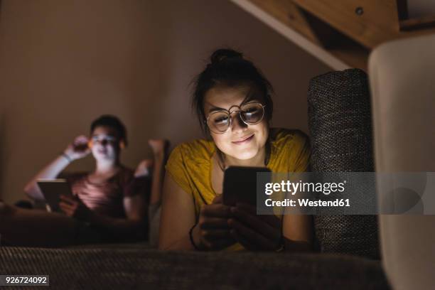 couple with cell phone and tablet relaxing on couch at home - 2 young woman on couch stock pictures, royalty-free photos & images