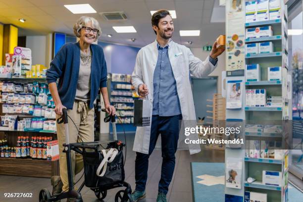 smiling pharmacist and customer with wheeled walker in pharmacy - rollator stock-fotos und bilder