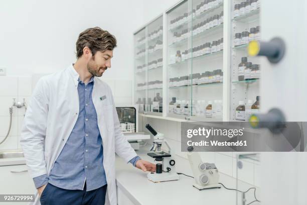 smiling man with microscope in laboratory - laborkittel stock-fotos und bilder